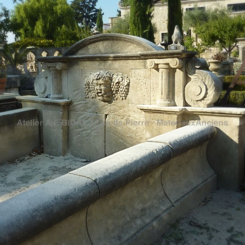 Wall fountain with long basin and pediment decorated with carved sculptures representing a hero of Roman mythology.